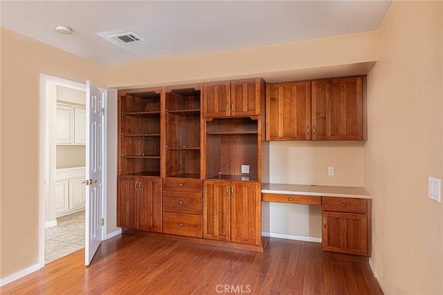 kitchen with baseboards, dark wood finished floors, visible vents, brown cabinetry, and built in desk