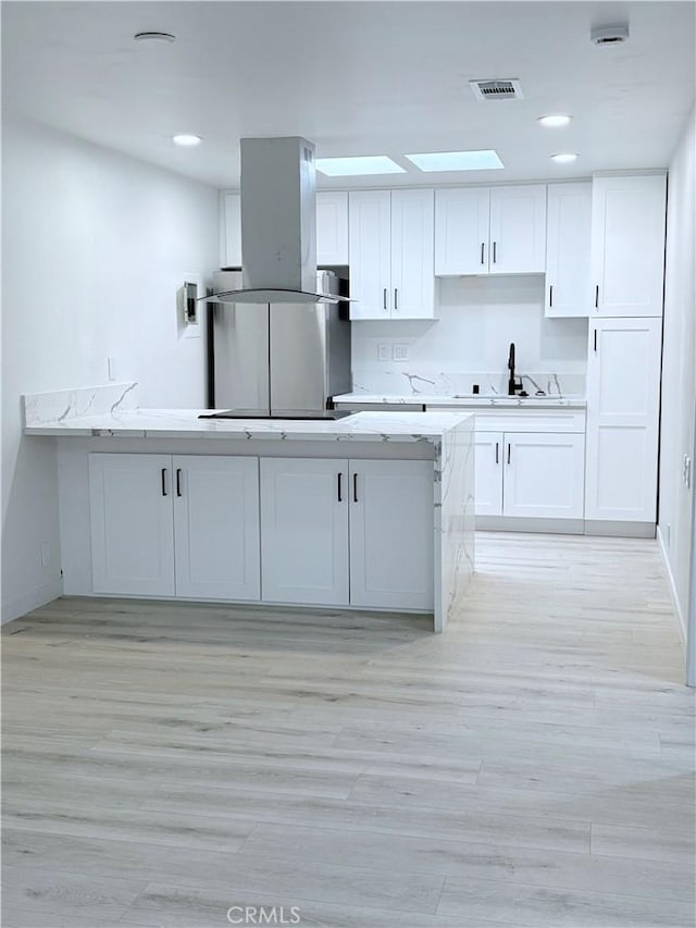 kitchen with visible vents, white cabinets, island exhaust hood, black electric cooktop, and a sink