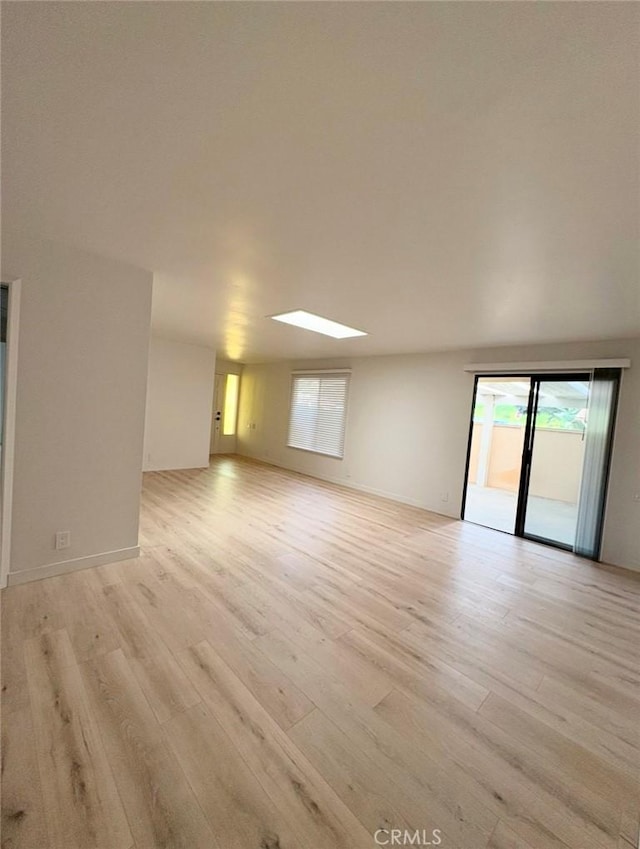 unfurnished room featuring a skylight, baseboards, and light wood finished floors