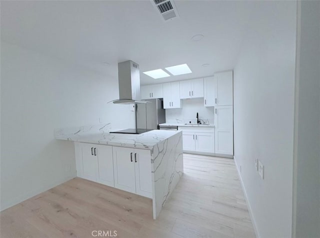 kitchen with black electric stovetop, island range hood, a peninsula, visible vents, and white cabinets