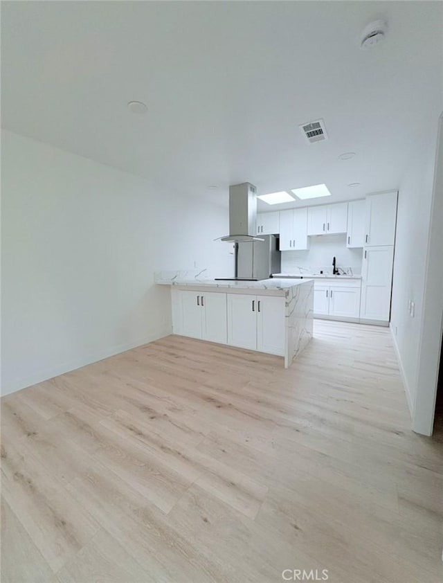 kitchen with visible vents, island range hood, a peninsula, light wood-type flooring, and white cabinetry