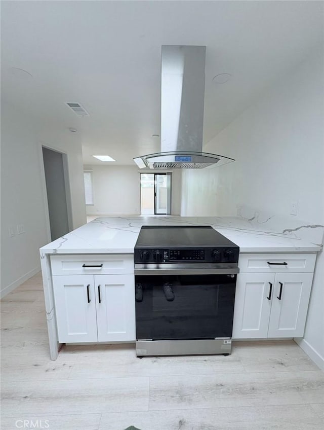 kitchen featuring light stone counters, island exhaust hood, electric range oven, white cabinets, and light wood-type flooring