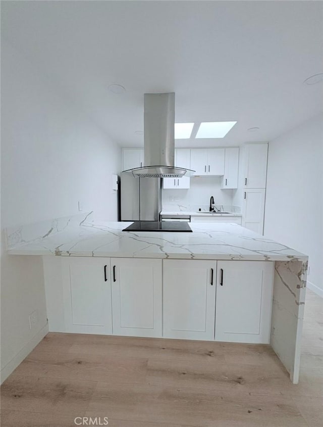 kitchen with light stone counters, a peninsula, white cabinetry, light wood-style floors, and island exhaust hood