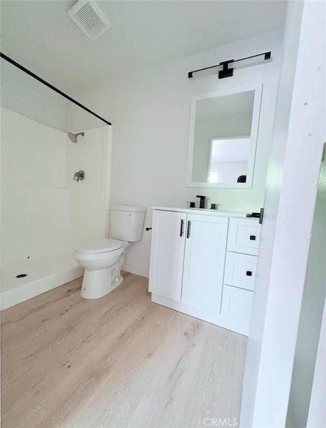 bathroom featuring visible vents, toilet, wood finished floors, walk in shower, and vanity