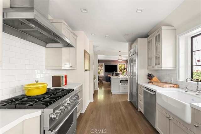 kitchen with premium appliances, wall chimney exhaust hood, dark wood-style flooring, light countertops, and a sink