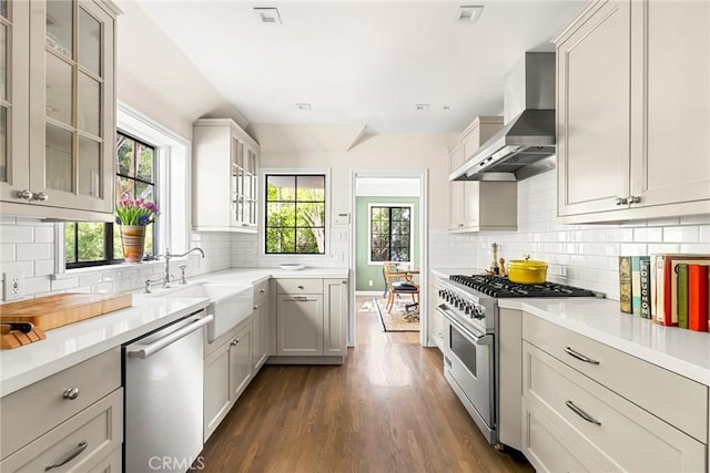 kitchen featuring appliances with stainless steel finishes, light countertops, a sink, and wall chimney range hood