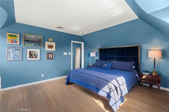 bedroom with vaulted ceiling, wood finished floors, visible vents, and baseboards