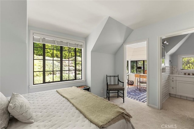 bedroom with light colored carpet, vaulted ceiling, ensuite bath, and a sink