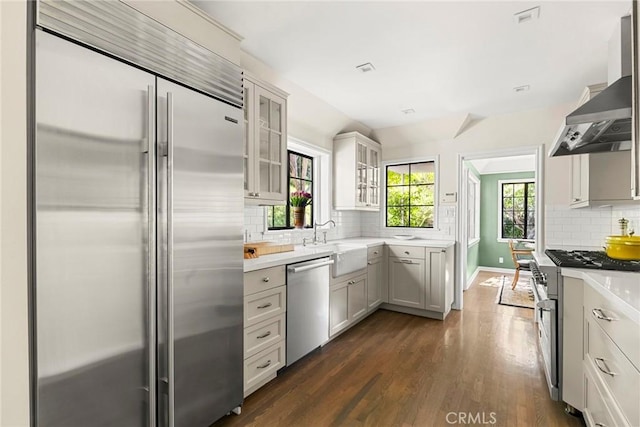 kitchen featuring dark wood finished floors, tasteful backsplash, light countertops, high quality appliances, and wall chimney exhaust hood