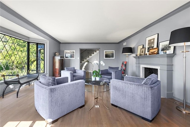 living area featuring stairs, a fireplace, crown molding, and wood finished floors