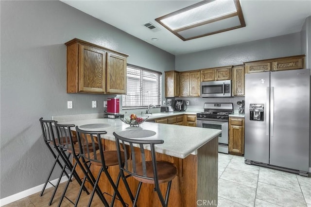 kitchen with stainless steel appliances, brown cabinetry, a peninsula, and visible vents