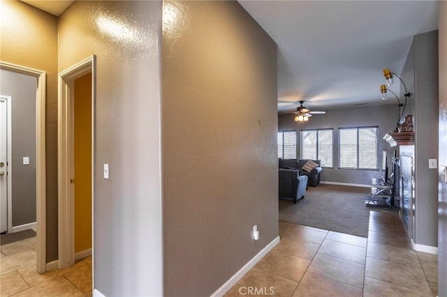 hallway featuring light carpet, baseboards, and light tile patterned floors