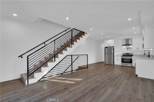 kitchen featuring wall chimney exhaust hood, appliances with stainless steel finishes, wood finished floors, white cabinetry, and a sink