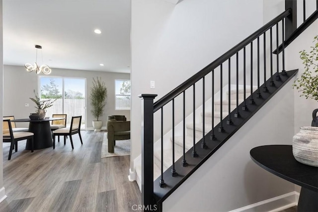 stairway featuring an inviting chandelier, baseboards, wood finished floors, and recessed lighting