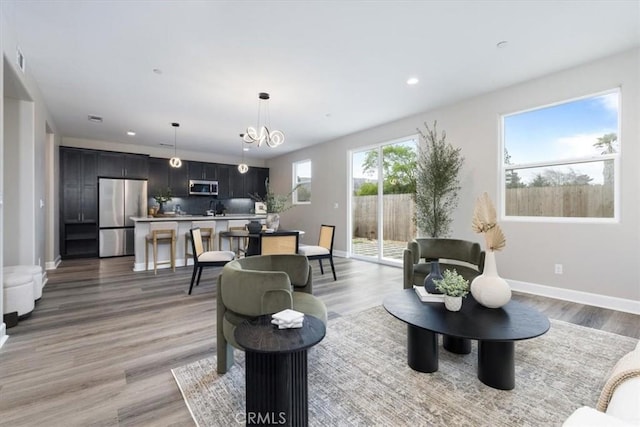 living area with baseboards, light wood-type flooring, a chandelier, and recessed lighting