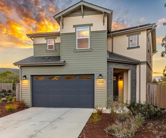 traditional home featuring an attached garage, fence, stone siding, concrete driveway, and roof with shingles