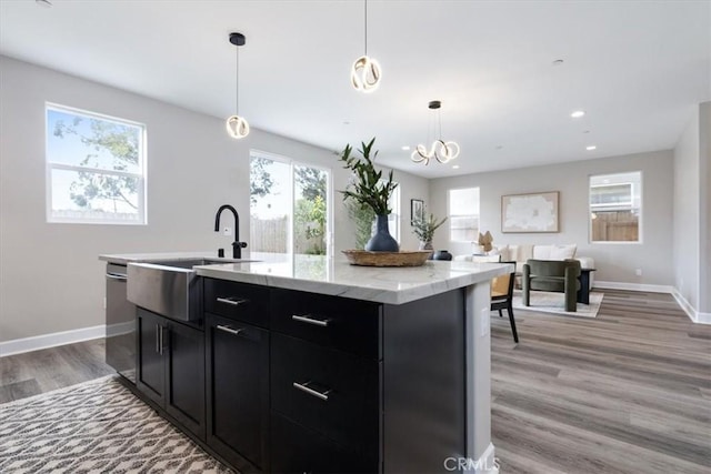 kitchen with dark cabinets, a sink, light wood-style flooring, and baseboards