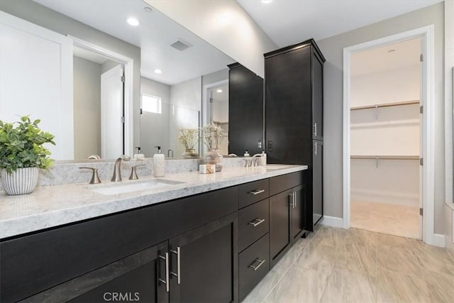 bathroom with double vanity, visible vents, a spacious closet, a sink, and baseboards