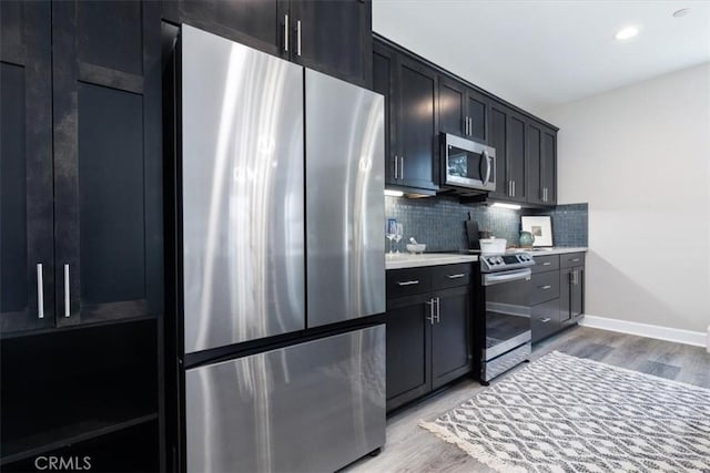 kitchen featuring baseboards, decorative backsplash, stainless steel appliances, light countertops, and light wood-type flooring