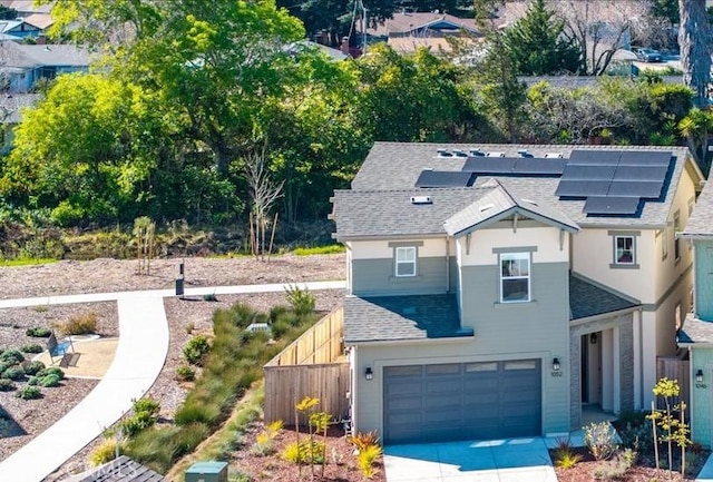 view of front of home featuring roof with shingles, concrete driveway, roof mounted solar panels, fence, and a garage