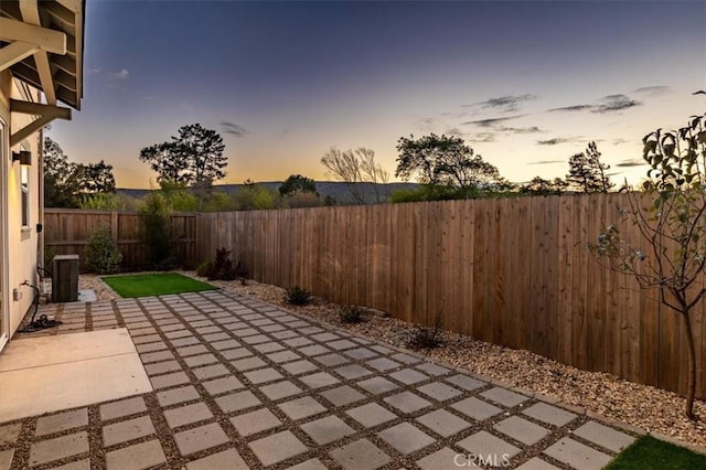 patio terrace at dusk featuring a fenced backyard and central AC