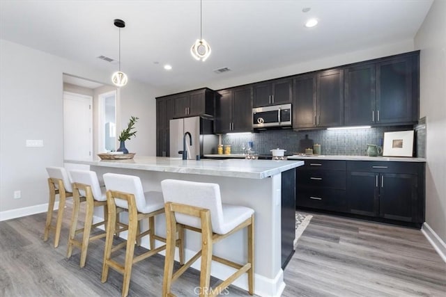 kitchen with stainless steel appliances, light countertops, tasteful backsplash, an island with sink, and a kitchen bar