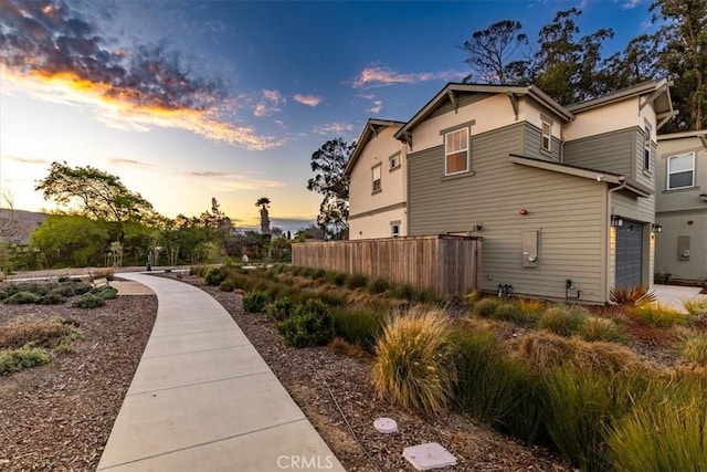 property exterior at dusk featuring a garage and fence