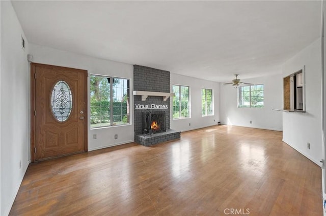 unfurnished living room with visible vents, a ceiling fan, a brick fireplace, wood finished floors, and baseboards