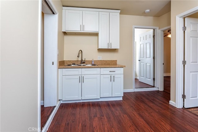 kitchen featuring dark wood-type flooring, a sink, white cabinetry, and light stone countertops