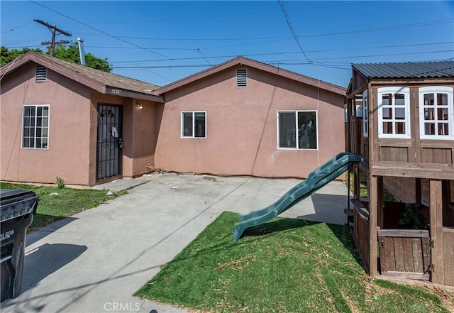 back of house with a lawn, a playground, and stucco siding