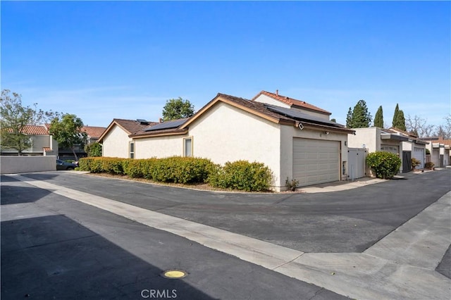 exterior space with a garage, roof mounted solar panels, a residential view, and stucco siding