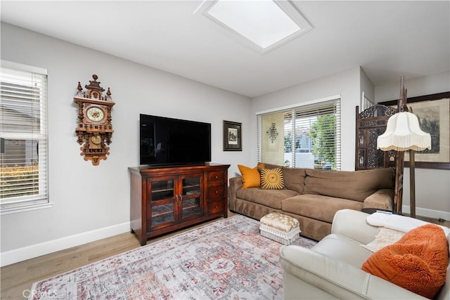 living area featuring a skylight, baseboards, and wood finished floors