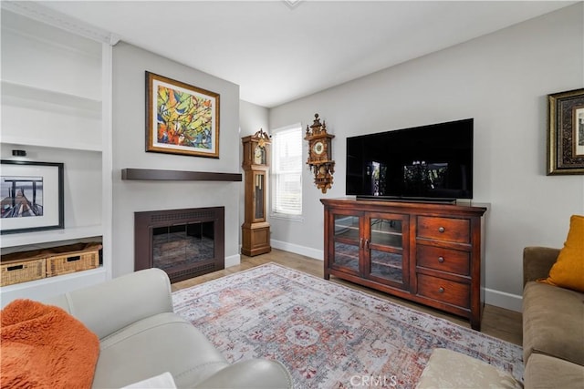 living room featuring built in features, a glass covered fireplace, baseboards, and wood finished floors