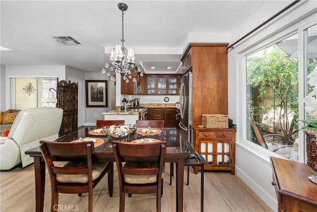 dining area with a chandelier, baseboards, visible vents, and light wood finished floors