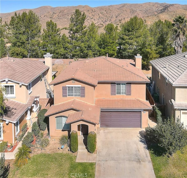 view of front of property featuring concrete driveway, a chimney, a tiled roof, an attached garage, and a mountain view