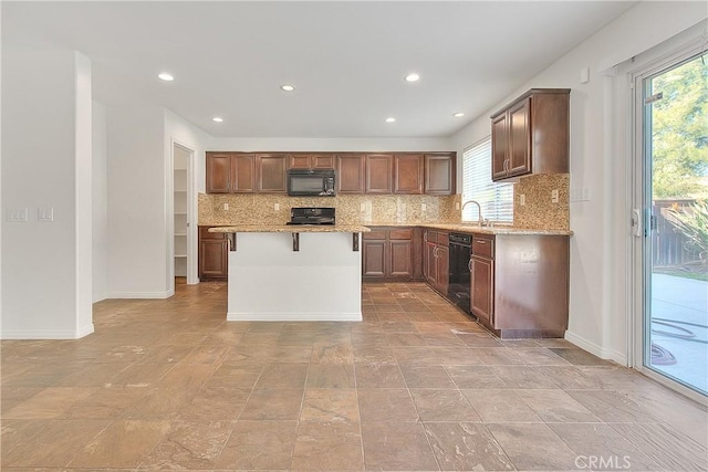 kitchen featuring backsplash, a kitchen island, black appliances, light stone countertops, and baseboards