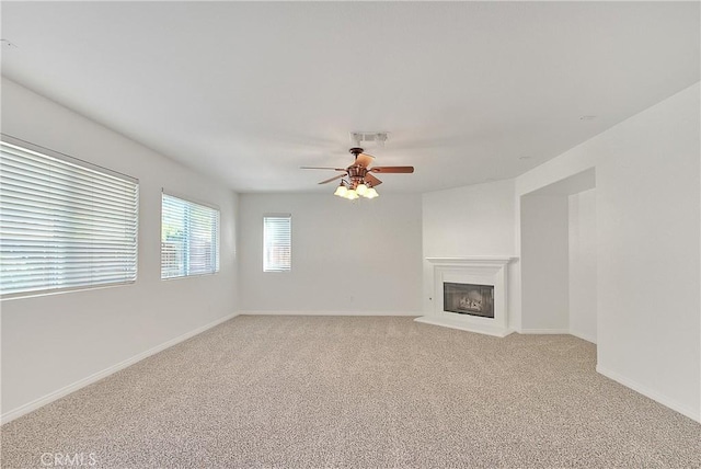 unfurnished living room with visible vents, a ceiling fan, a glass covered fireplace, light carpet, and baseboards