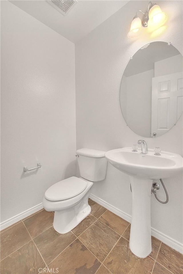 half bathroom with toilet, visible vents, and baseboards