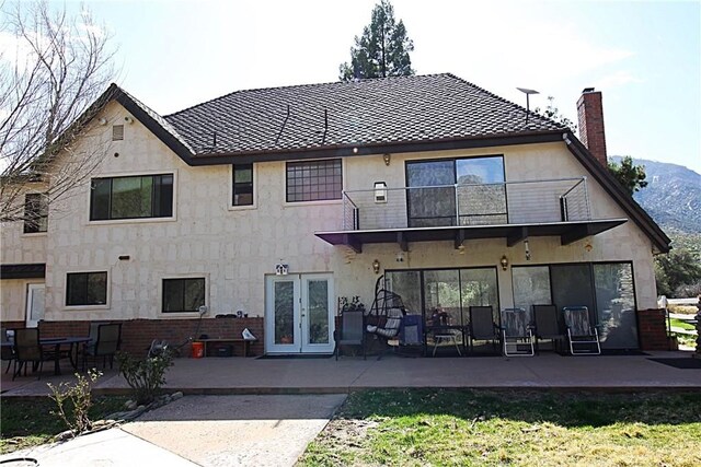 rear view of property with a balcony, stucco siding, a patio, and french doors