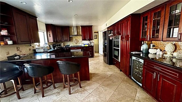 kitchen with beverage cooler, a peninsula, wall chimney range hood, freestanding refrigerator, and reddish brown cabinets