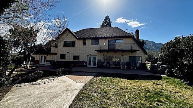 rear view of house featuring french doors, a patio, a balcony, and a lawn