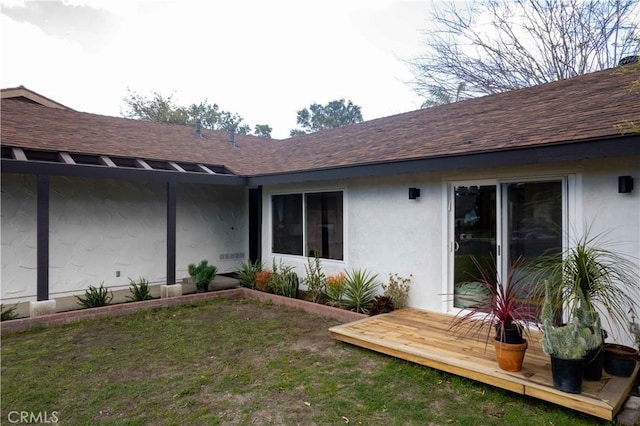 view of exterior entry with roof with shingles, a lawn, and stucco siding