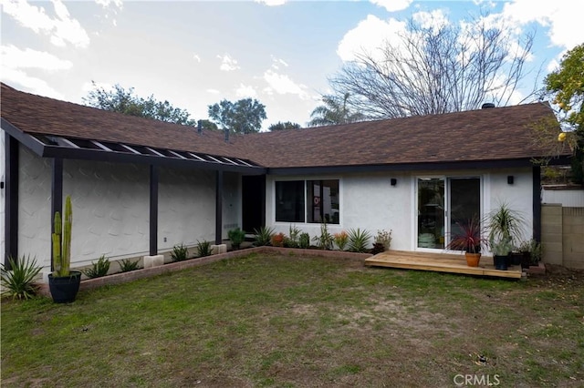 exterior space featuring stucco siding, roof with shingles, a deck, and a yard