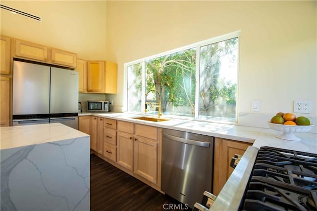 kitchen featuring visible vents, light stone countertops, stainless steel appliances, light brown cabinetry, and a sink