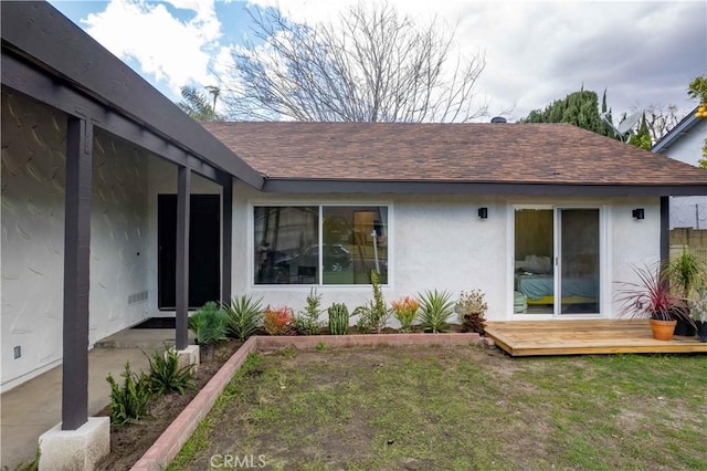 rear view of house with a shingled roof, a lawn, a deck, and stucco siding