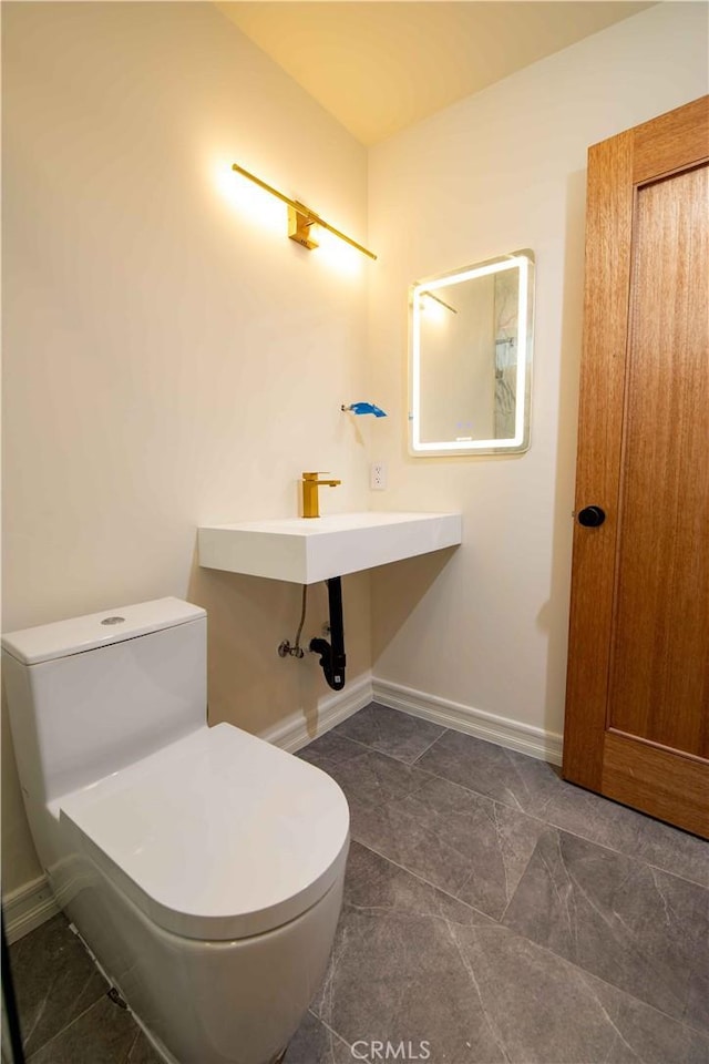 half bathroom featuring baseboards, a sink, and toilet