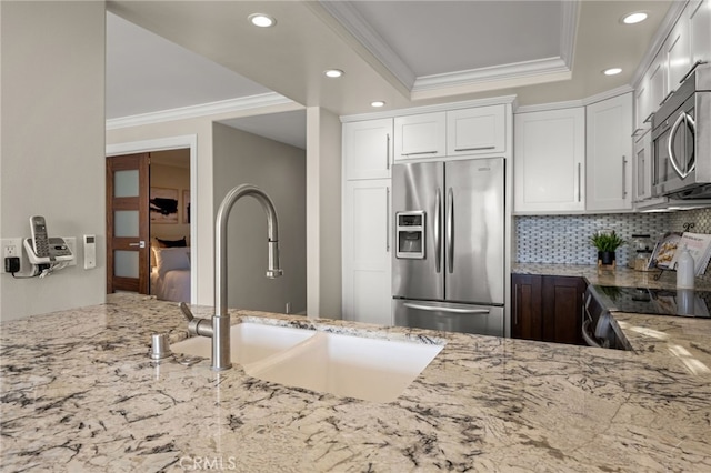 kitchen featuring appliances with stainless steel finishes, a sink, ornamental molding, and light stone countertops