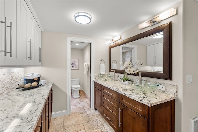 full bathroom with double vanity, baseboards, toilet, stone tile flooring, and a sink