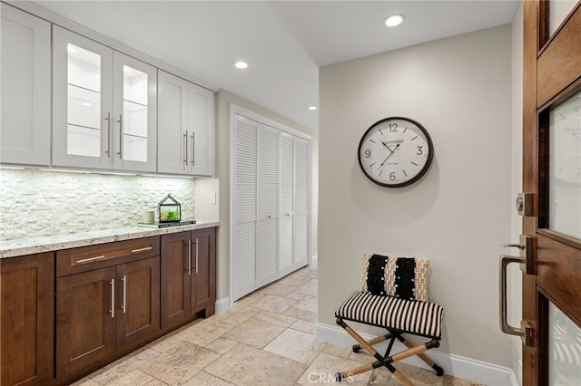 interior space with glass insert cabinets, backsplash, stone tile flooring, and baseboards