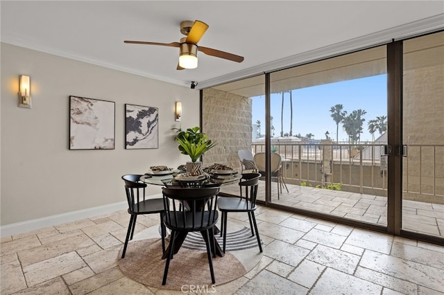 dining area featuring floor to ceiling windows, stone tile flooring, ornamental molding, a ceiling fan, and baseboards